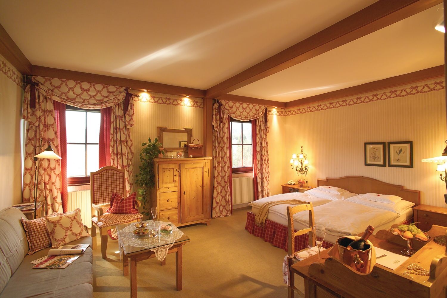 Útulný hotelový pokoj ve venkovském stylu s manželskou postelí, pohovkou, stolem a rustikálním dřevěným nábytkem.