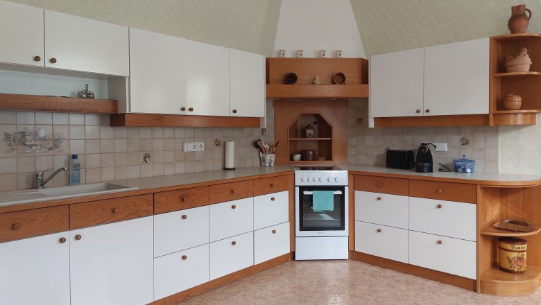 Kuchyň s b&iacute;l&yacute;mi a dřevěn&yacute;mi skř&iacute;ňkami, spor&aacute;kem a dřezem.