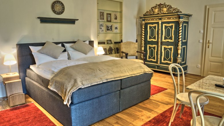 Elegantní ložnice s manželskou postelí, starožitnou skříní a červenými koberci.