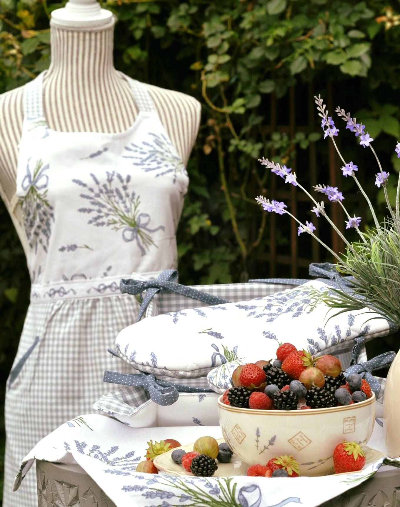 Mísa s bobulemi na stole s levandulovými dekoracemi a krejčovská figurína se zástěrou v pozadí.