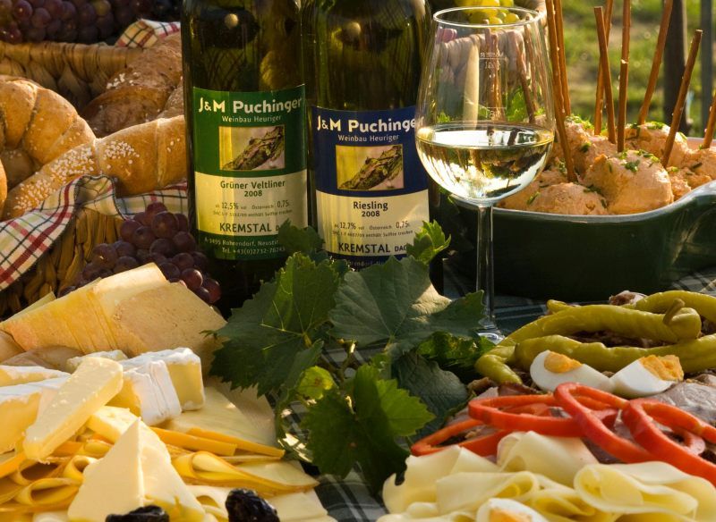 Občerstvení Heurigen s vínem, sýrem, chlebem a uzeninami na stole.