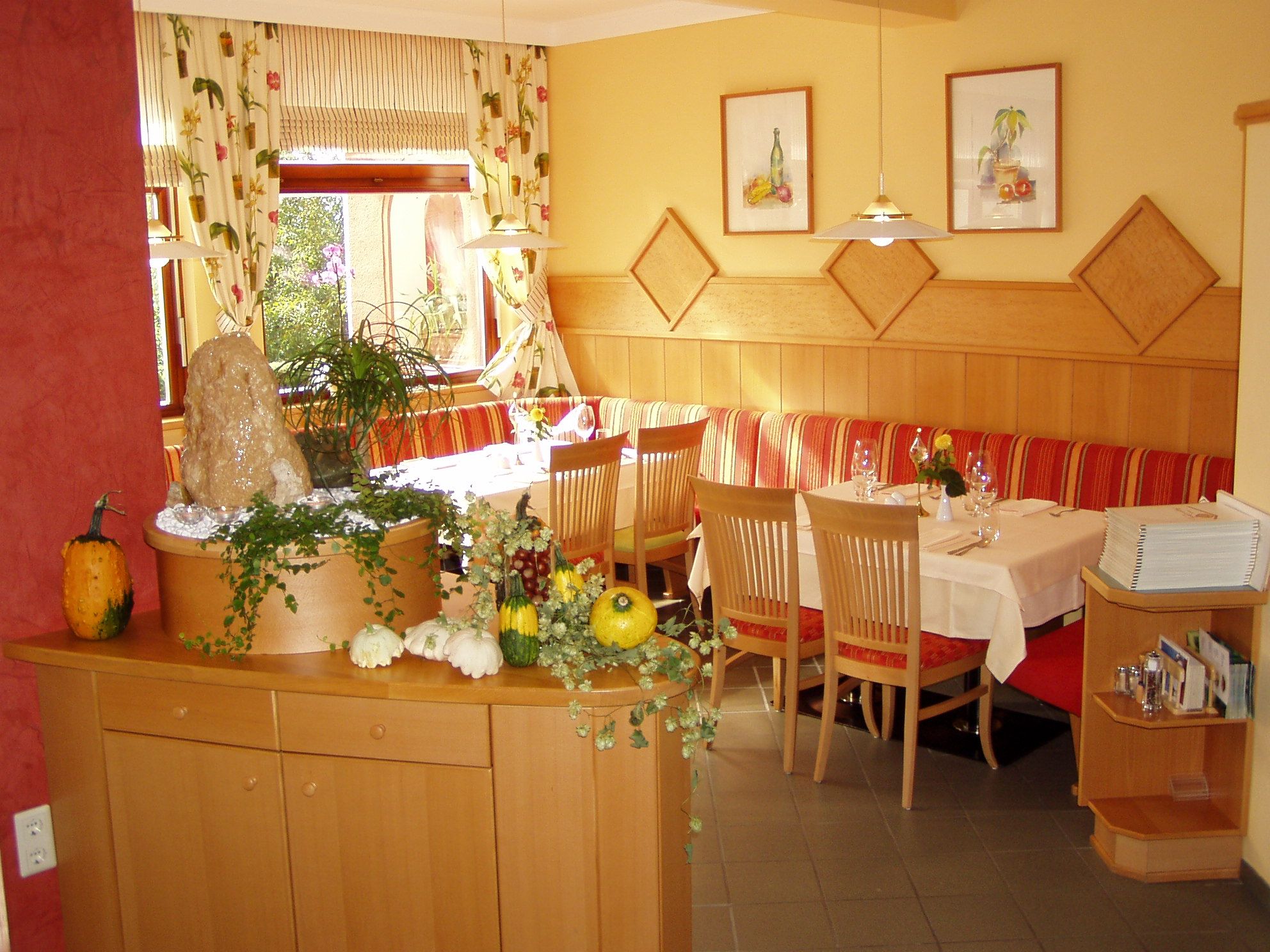 Útulná restaurace s dřevěným nábytkem, vyzdobená dýněmi a rostlinami.