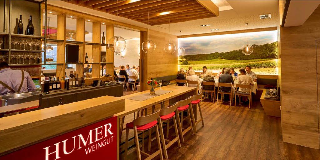 Pohled do interiéru moderní vinárny s dřevěným nábytkem a velkou fototapetou vinice.