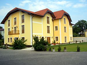 Žlutá dvoupatrová budova s červenou střechou a udržovanou zahradou.