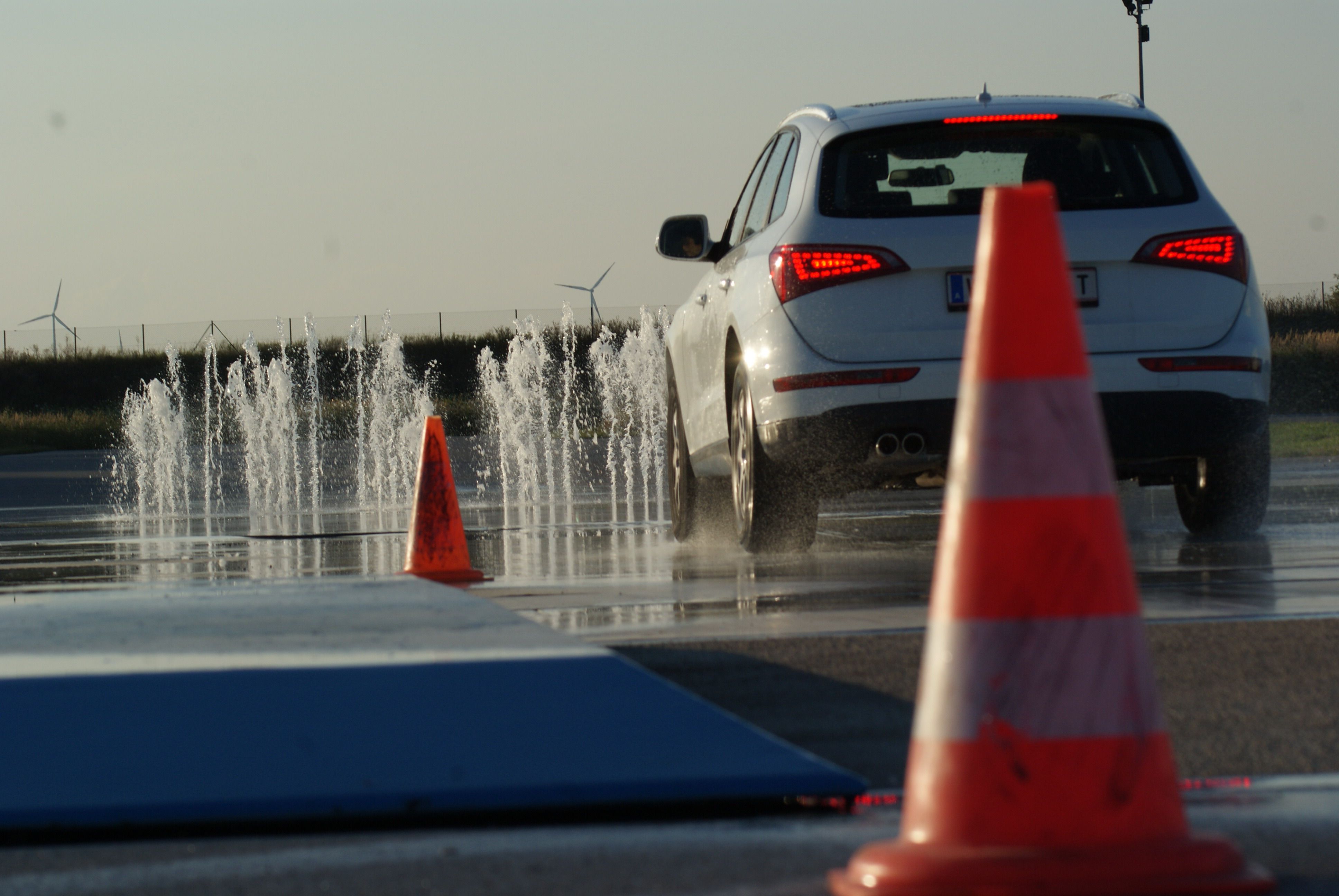 Auto jede po mokré vozovce s vodními fontánami a dopravními kužely.
