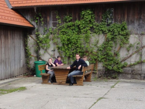 Čtyři lidé sedí u dřevěného stolu před budovou porostlou břečťanem.