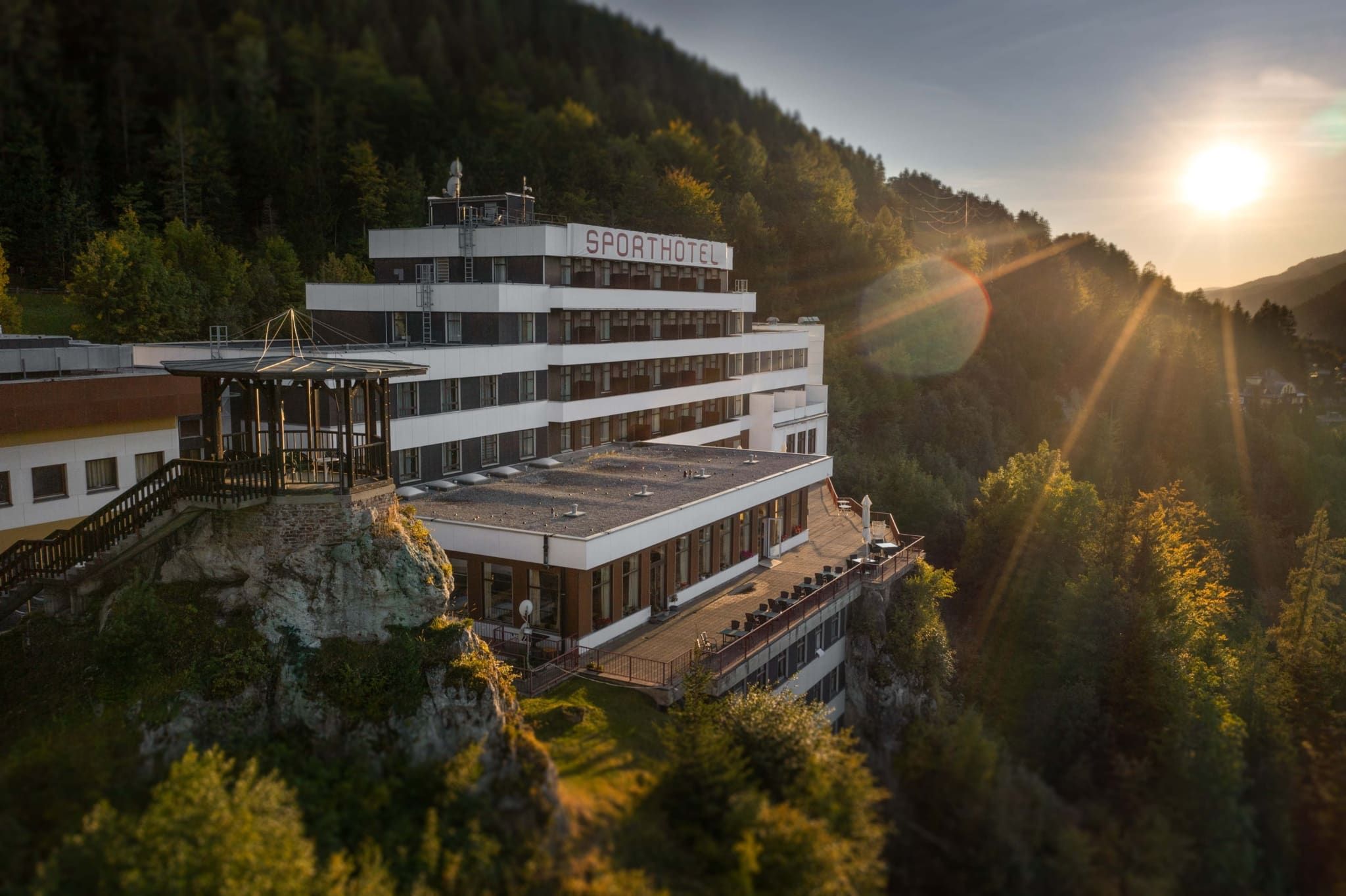 Hotel na kopci při západu slunce obklopený lesem.