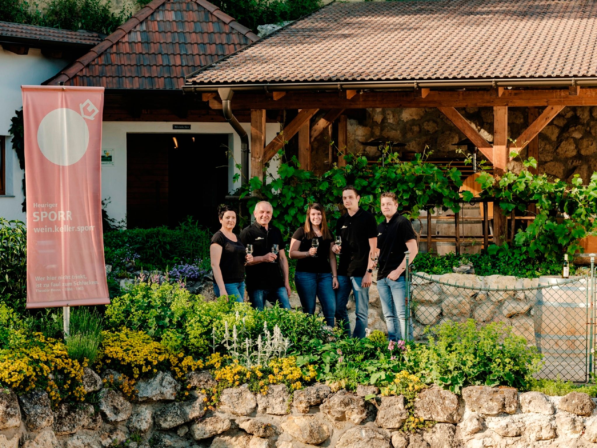 Skupina pěti lidí před vinařstvím s transparentem Sporr.