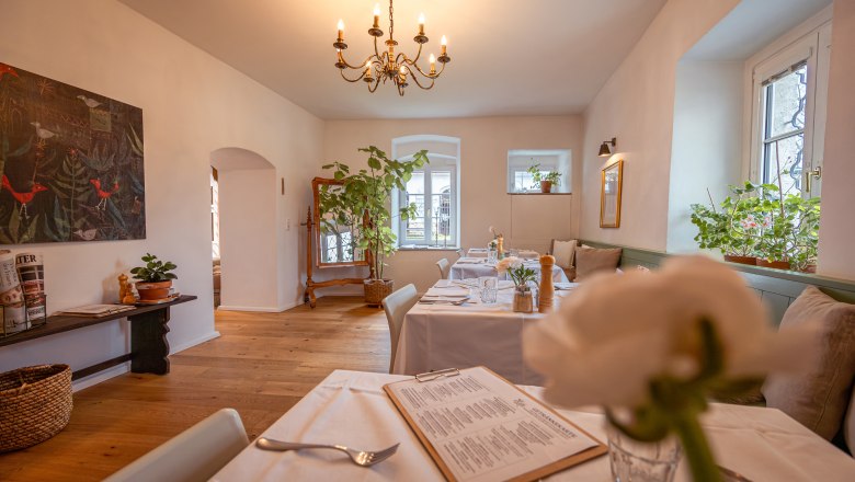 &Uacute;tuln&aacute; restaurace s dřevěnou podlahou, b&iacute;l&yacute;mi ubrusy a rostlinami.