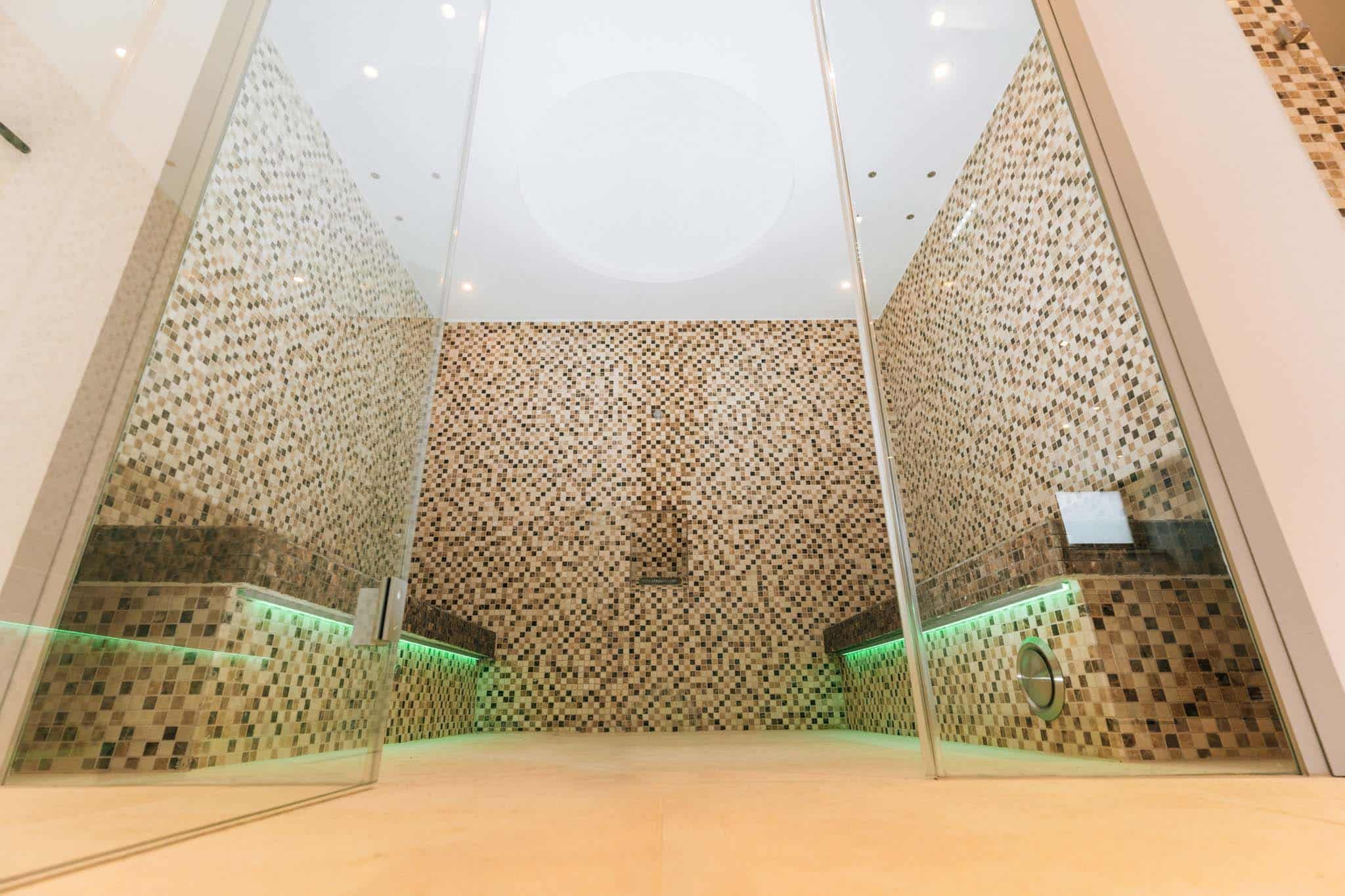 Moderní sauna s mozaikovými obklady a skleněnými stěnami.