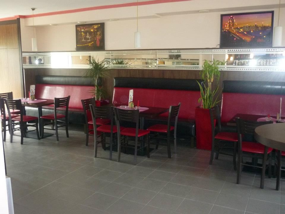 Pohled do interiéru kavárny s červenými lavicemi a černými židlemi.