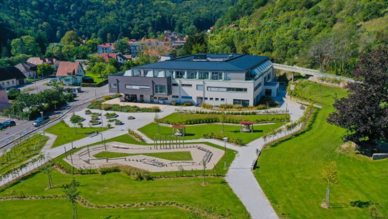 Leteck&yacute; pohled na modern&iacute; budovu se zahradou obklopenou zelen&yacute;mi kopci.