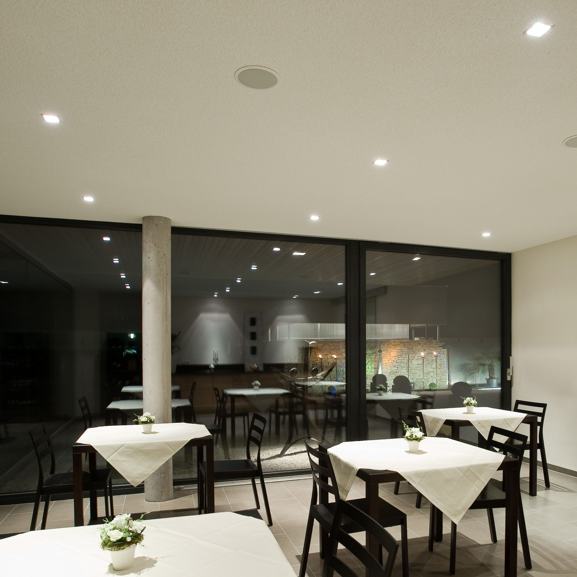 Moderní snídaňová místnost se stoly a židlemi, zdobená bílými ubrusy a květinami.