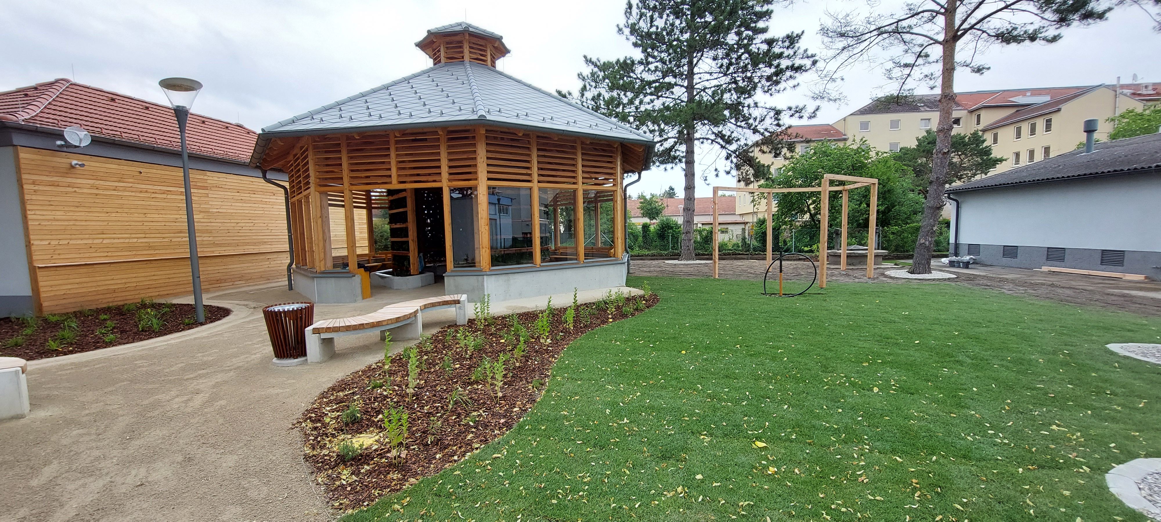 Moderní inhalatorium s dřevěnou konstrukcí a prosklenými okny v udržované zahradě s trávníkem a stromy.