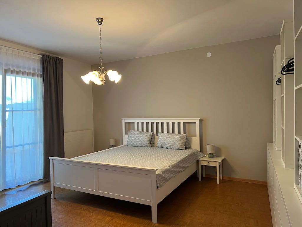 Ložnice s bílou postelí, nočním stolkem a šatní skříní.