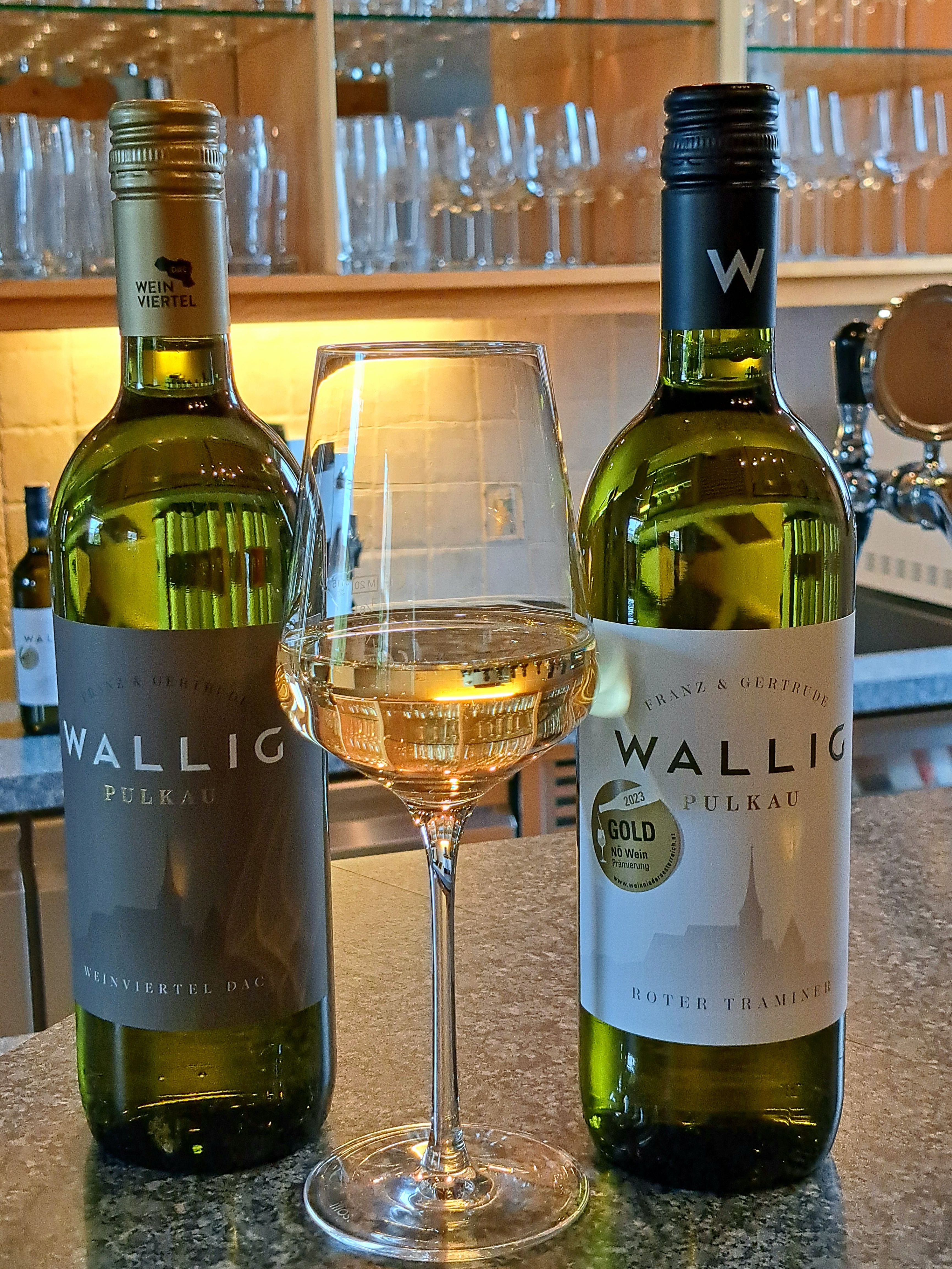 Dvě láhve vína a sklenice bílého vína na pultu.