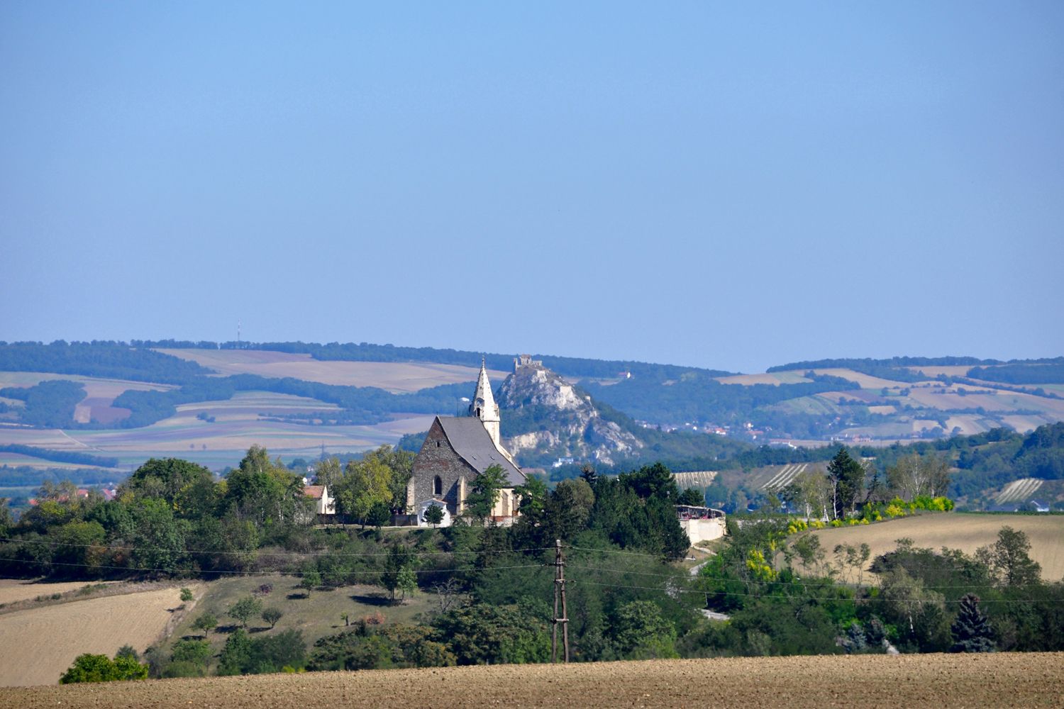 Krajina s kostelem a kopcem v pozadí.