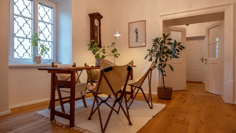 &Uacute;tuln&yacute; pokoj s dřevěnou podlahou, stolem, židlemi a rostlinami.