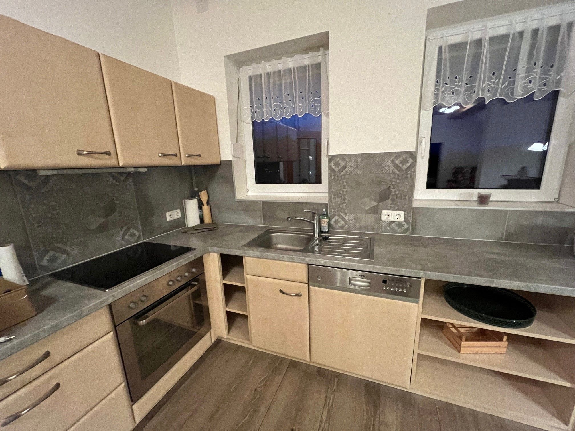 Moderní kuchyně s dřevěnými skříňkami, elektrickým sporákem, dřezem a myčkou nádobí.