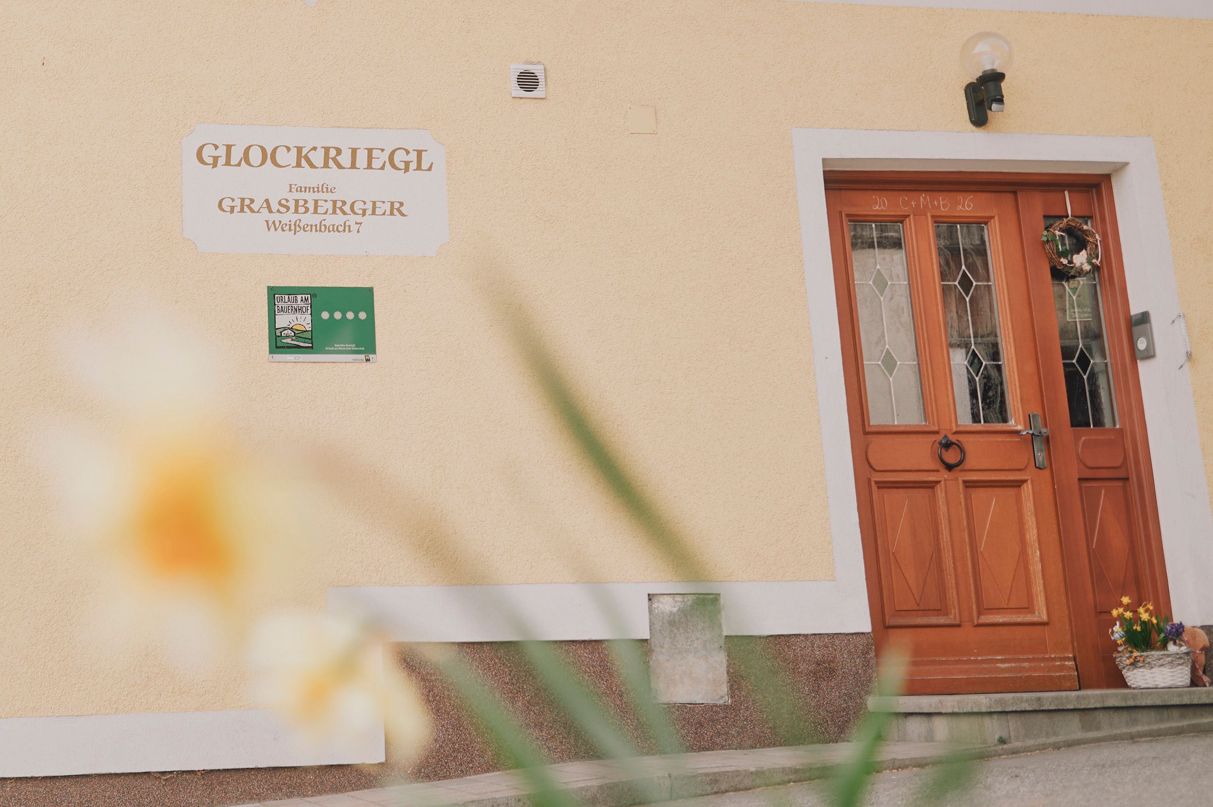 Vchod do domu s dřevěnými dveřmi a nápisem "Glockriegl" na zdi.