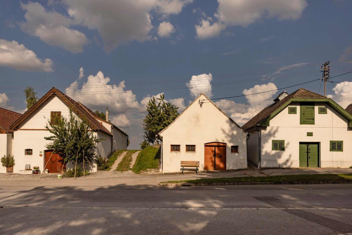 Tři tradiční sklepní domky v Kettlasbrunnu pod modrou oblohou s mraky.