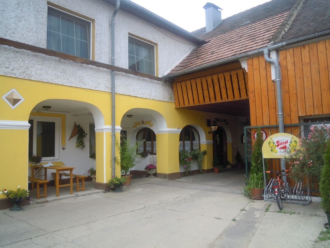Žlutý arkádový dvůr s dřevěnou střechou a rostlinami.
