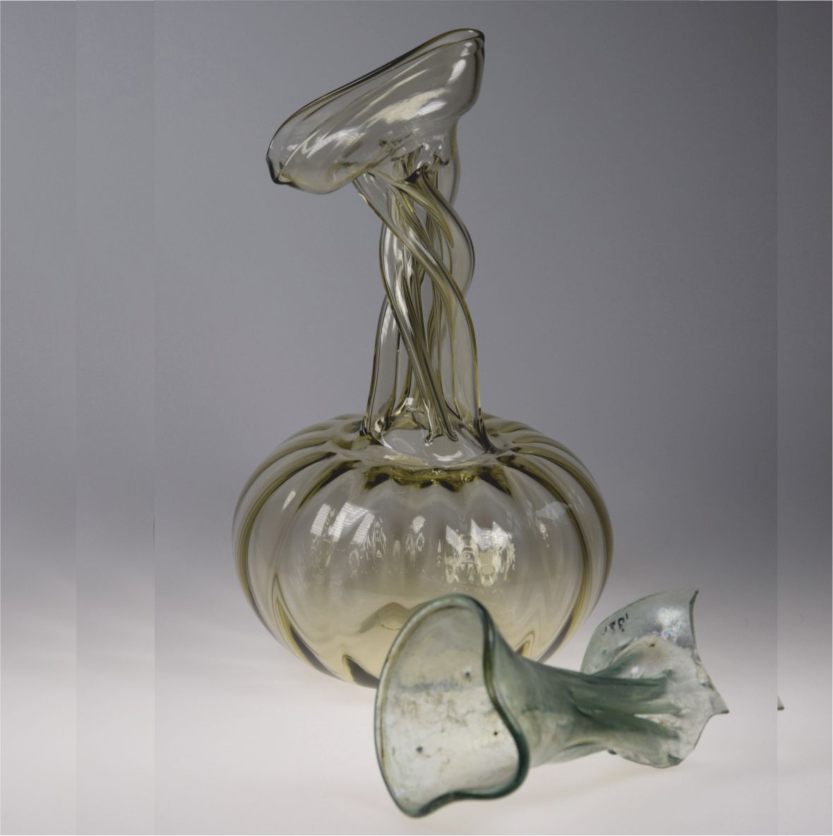 Skleněný objekt s pokroucenými tvary na šedém pozadí.