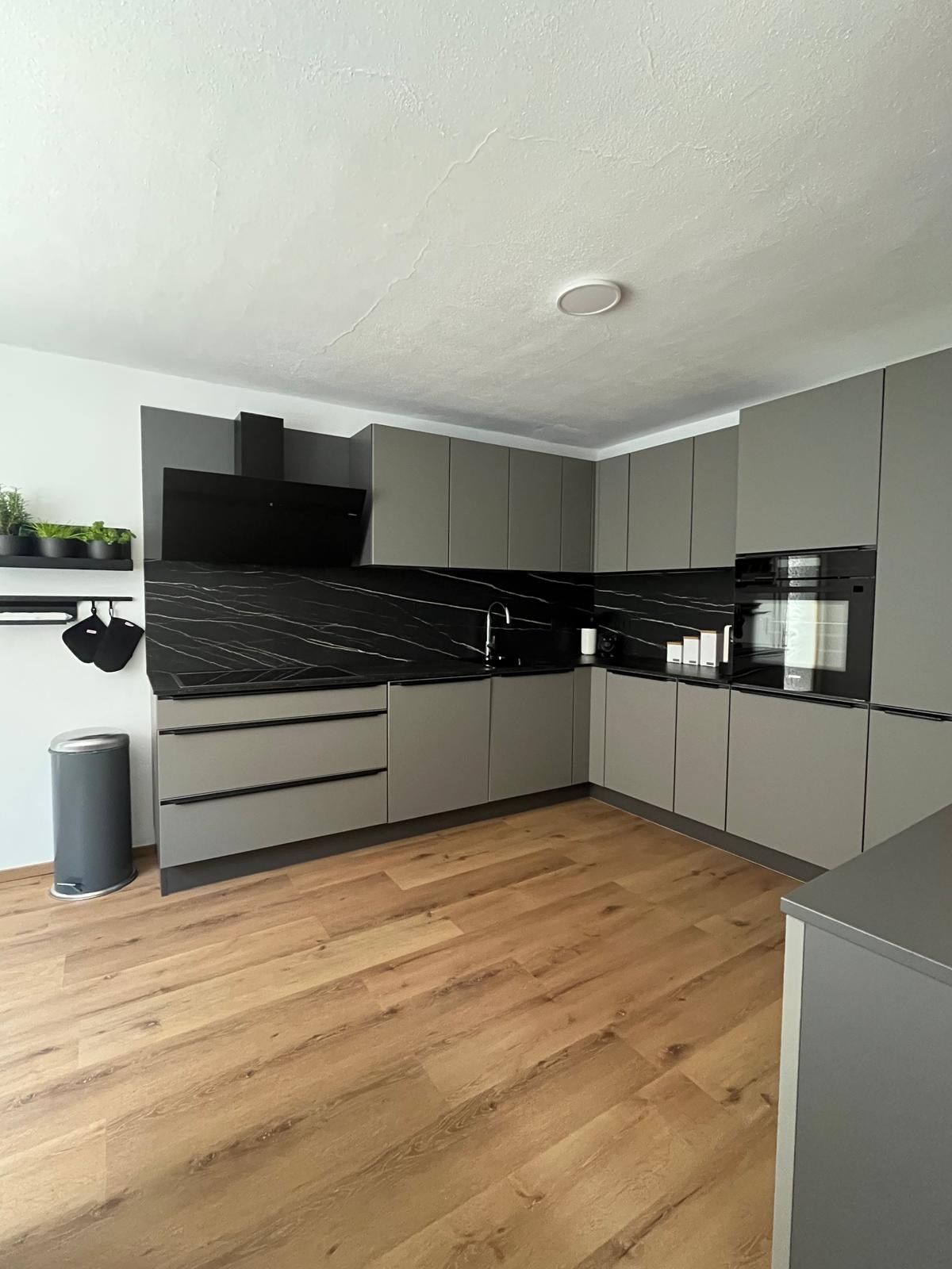 Moderní šedá kuchyňská linka s černou pracovní deskou a dřevěnou podlahou.