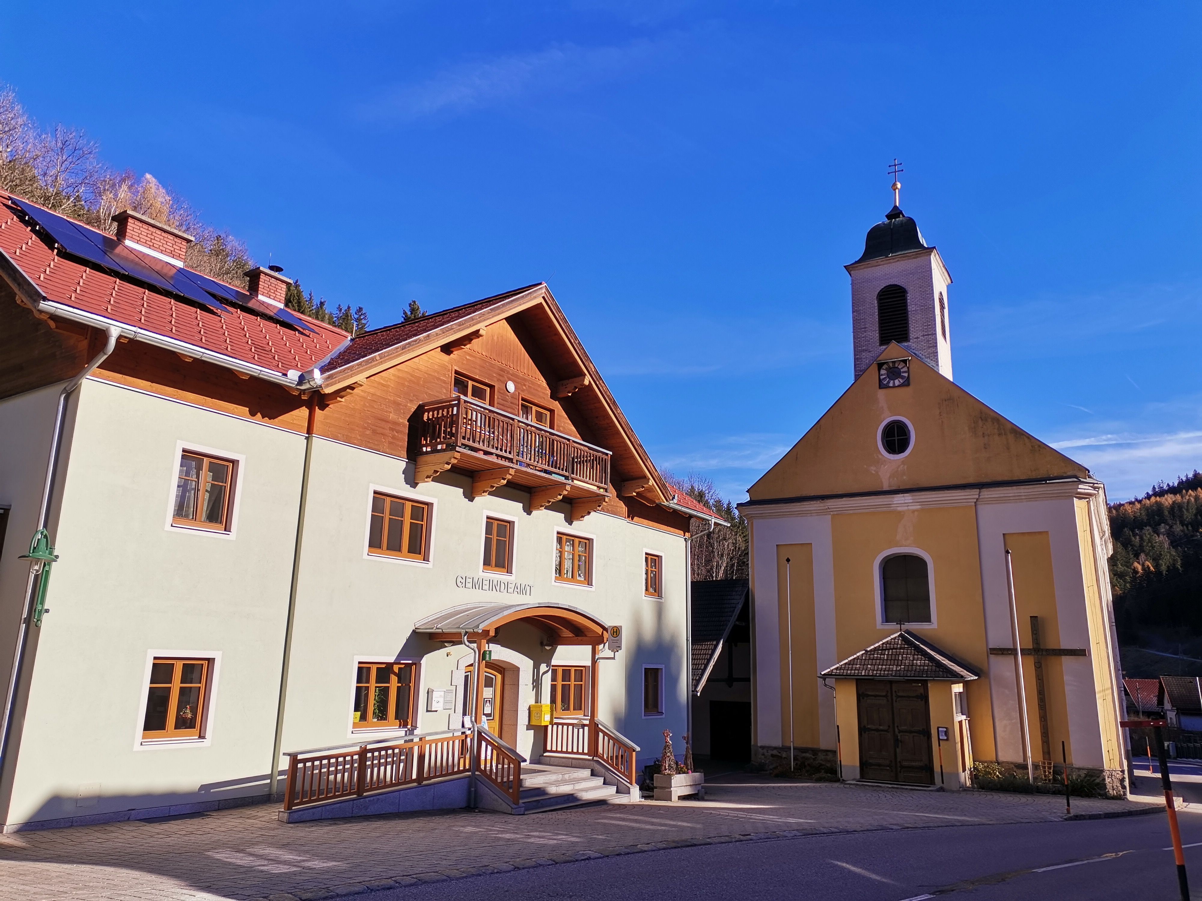 Obecní úřad a kostel v Trattenbachu za slunečného počasí.