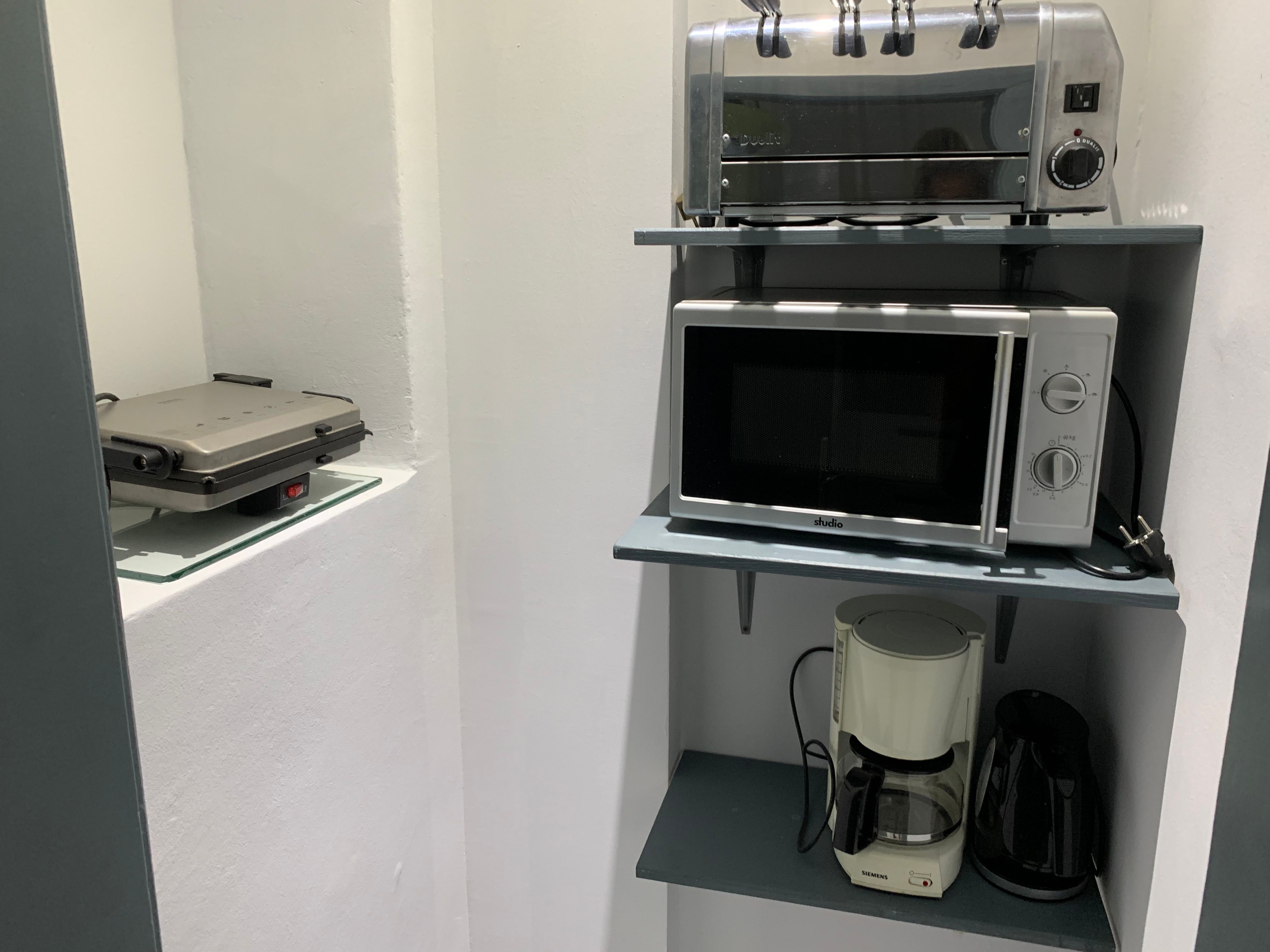Kuchyňská polička s toustovačem, mikrovlnnou troubou, kávovarem a rychlovarnou konvicí.