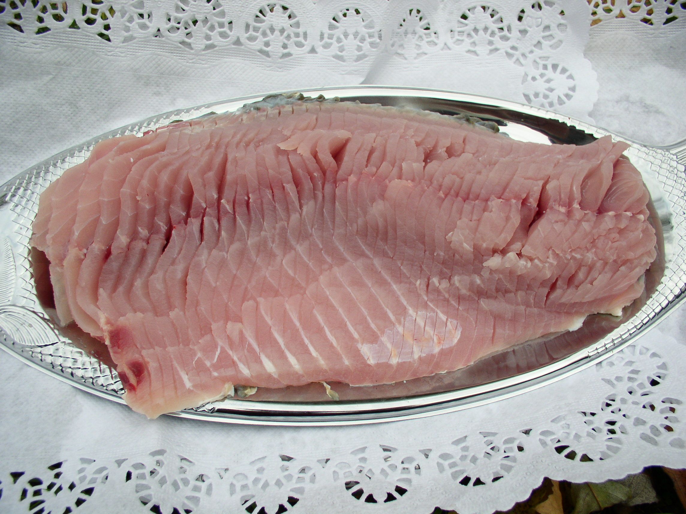 Syrový filet z kapra na stříbrném podnose, obklopený krajkovým papírem.