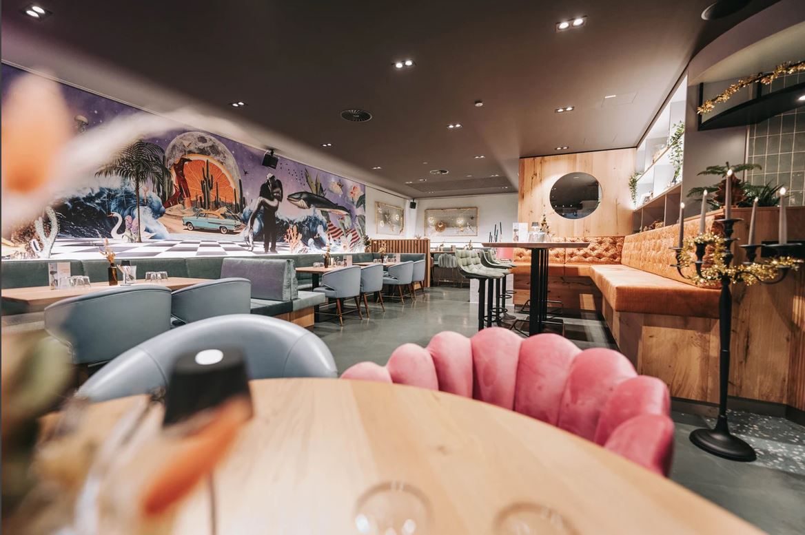 Pohled do interiéru stylové restaurace s moderním nábytkem a uměleckými díly na stěnách.