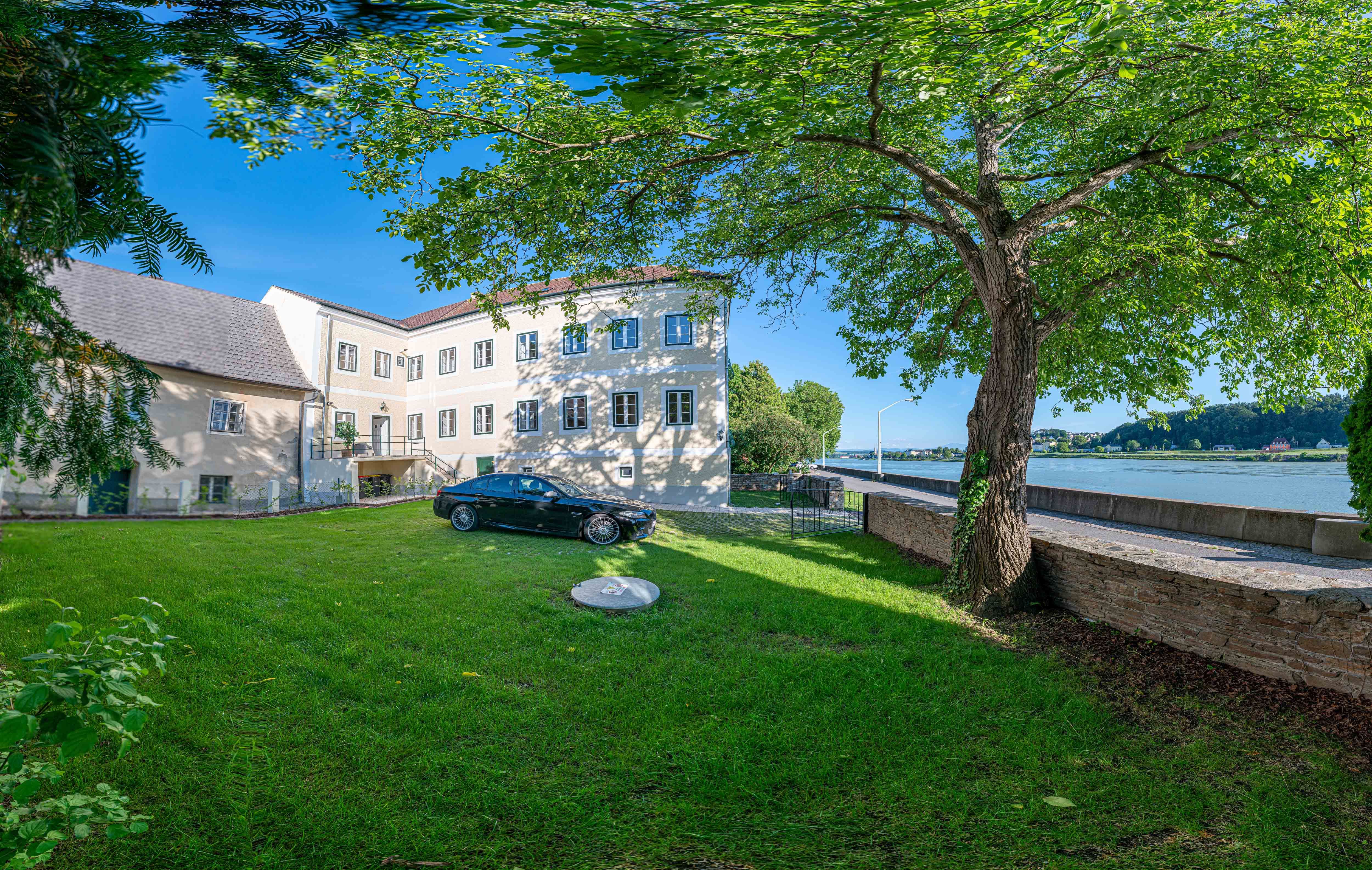 Pohled zvenčí na starou poštu se stromem a autem v popředí, v pozadí Dunaj.