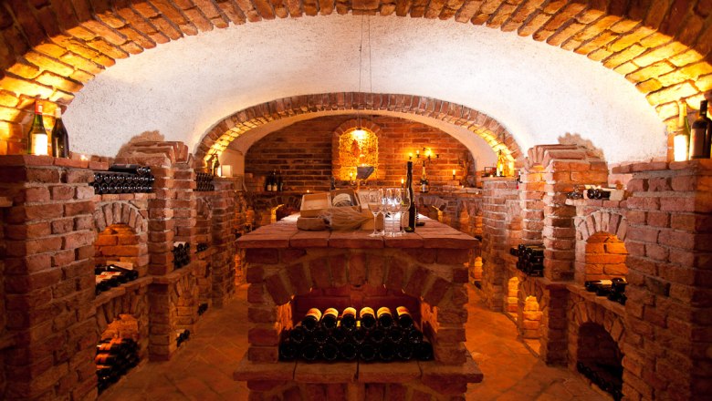 Atmosf&eacute;ricky osvětlen&yacute; vinn&yacute; sklep s cihlov&yacute;mi zdmi a lahvemi v&iacute;na na polic&iacute;ch.