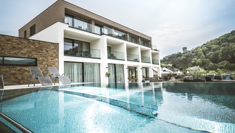 Moderní butikový hotel s bazénem a lehátky, obklopený zelenou krajinou.