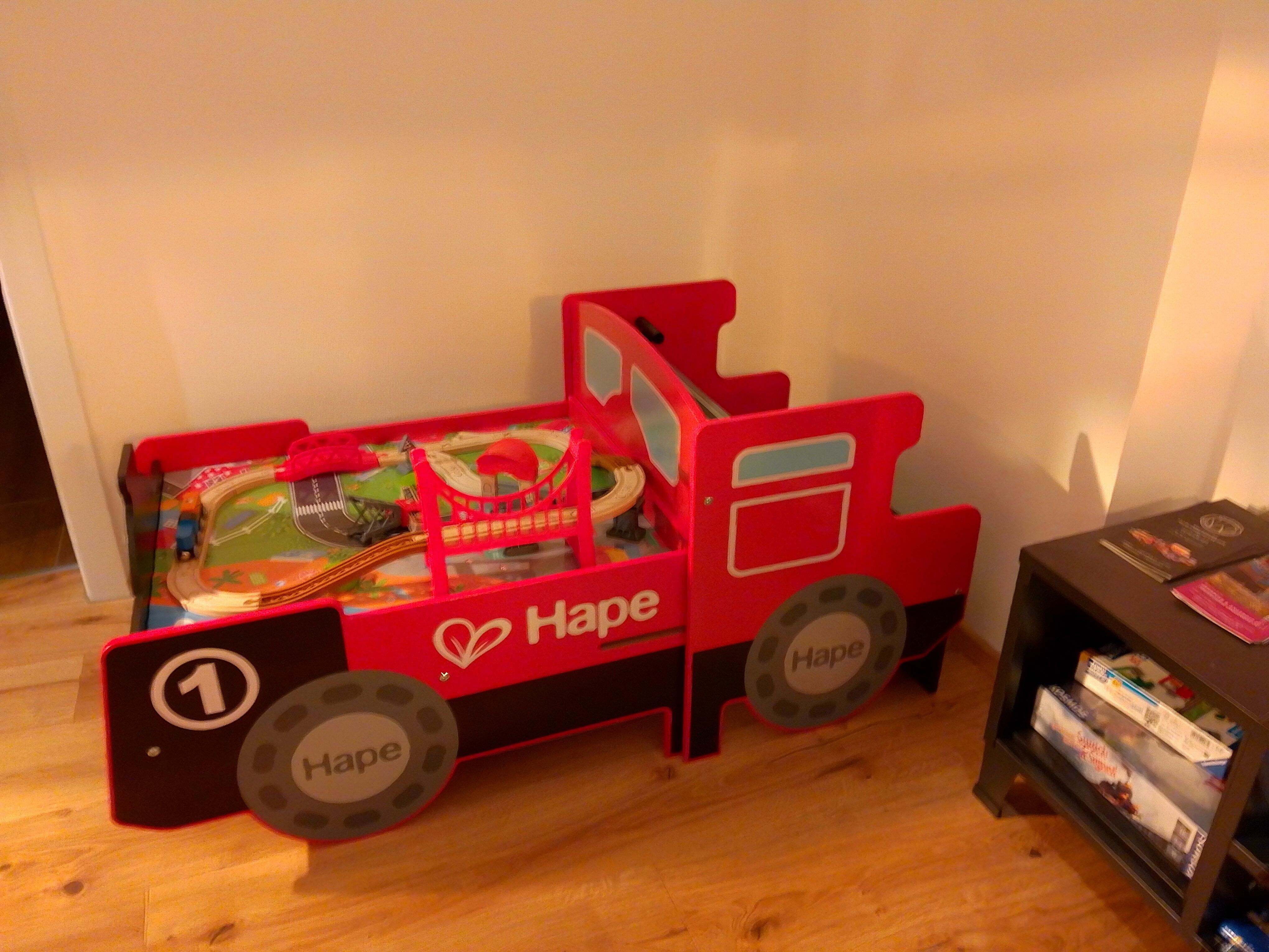 Červená hračková postel ve tvaru lokomotivy s hračkovou železnicí.