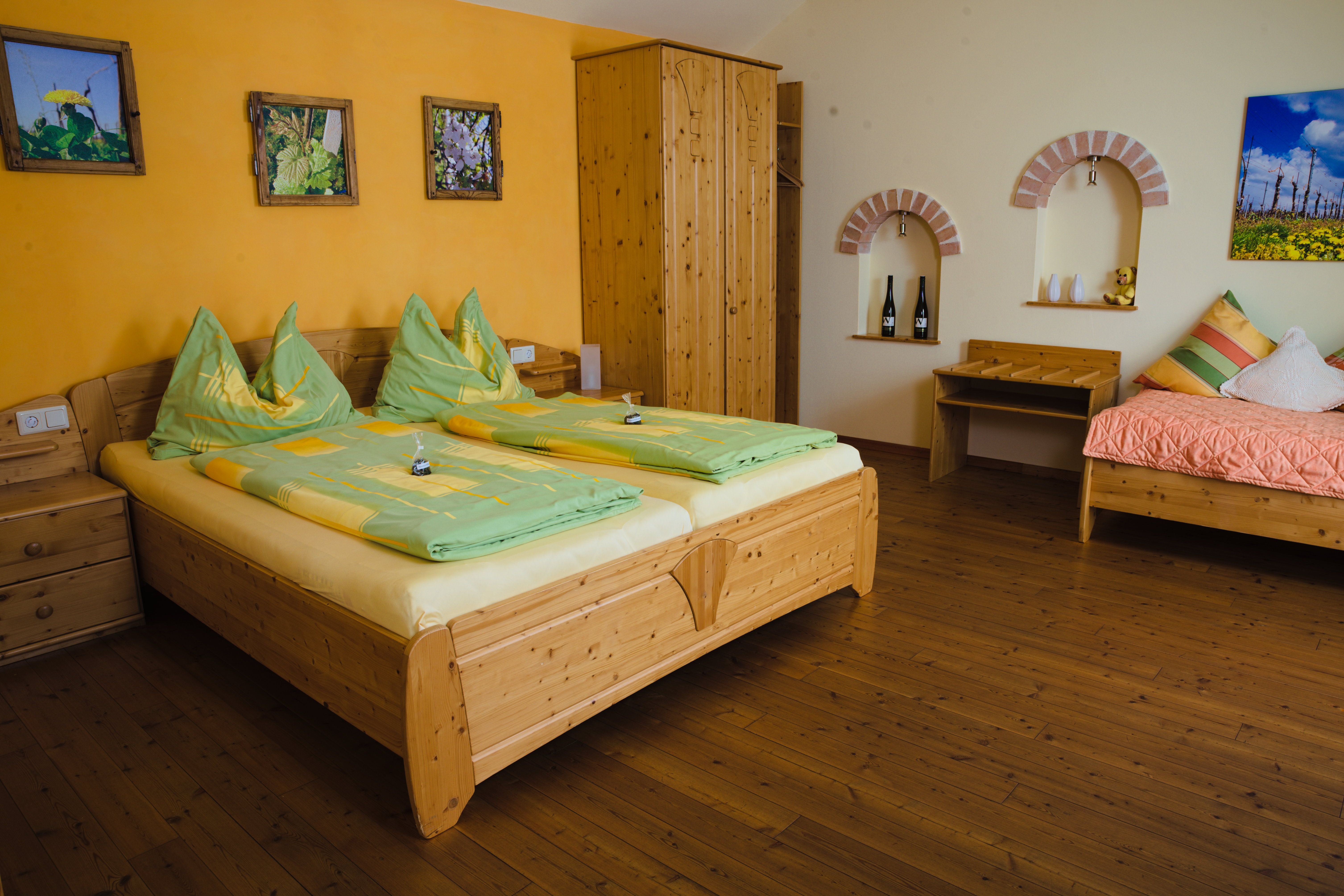 Útulný pokoj pro hosty s dřevěným nábytkem, manželskou postelí, samostatným lůžkem a dekorativními obrázky na stěně.