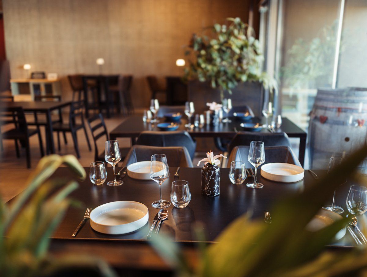 Elegantní restaurace s prostřenými stoly, sklenicemi na víno a rostlinami v pozadí.