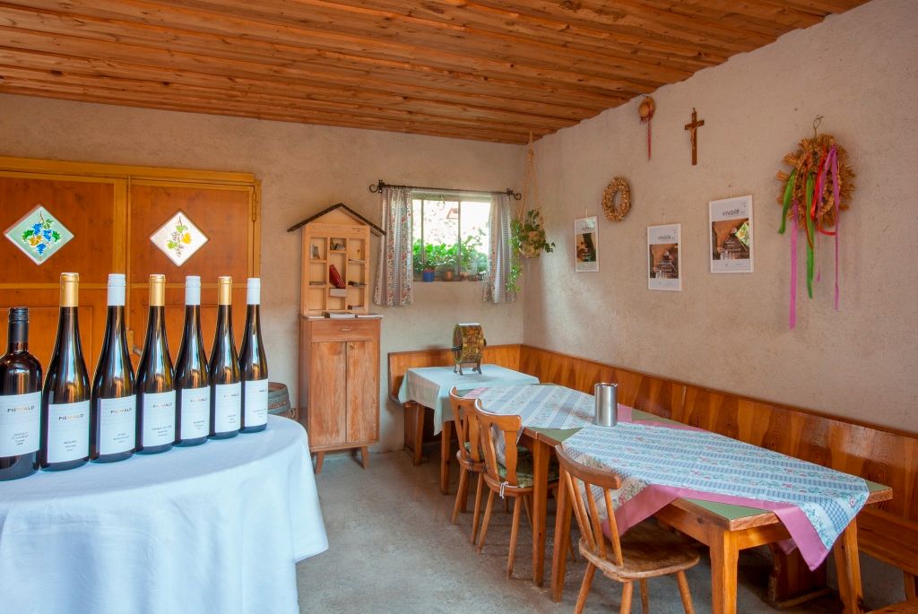 Degustační místnost vinařství Piewald s lahvemi vína na stole a rustikálním nábytkem.