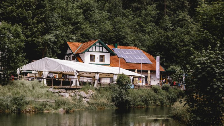 Hostinec se solárními panely a stanem na okraji lesa u rybníka.
