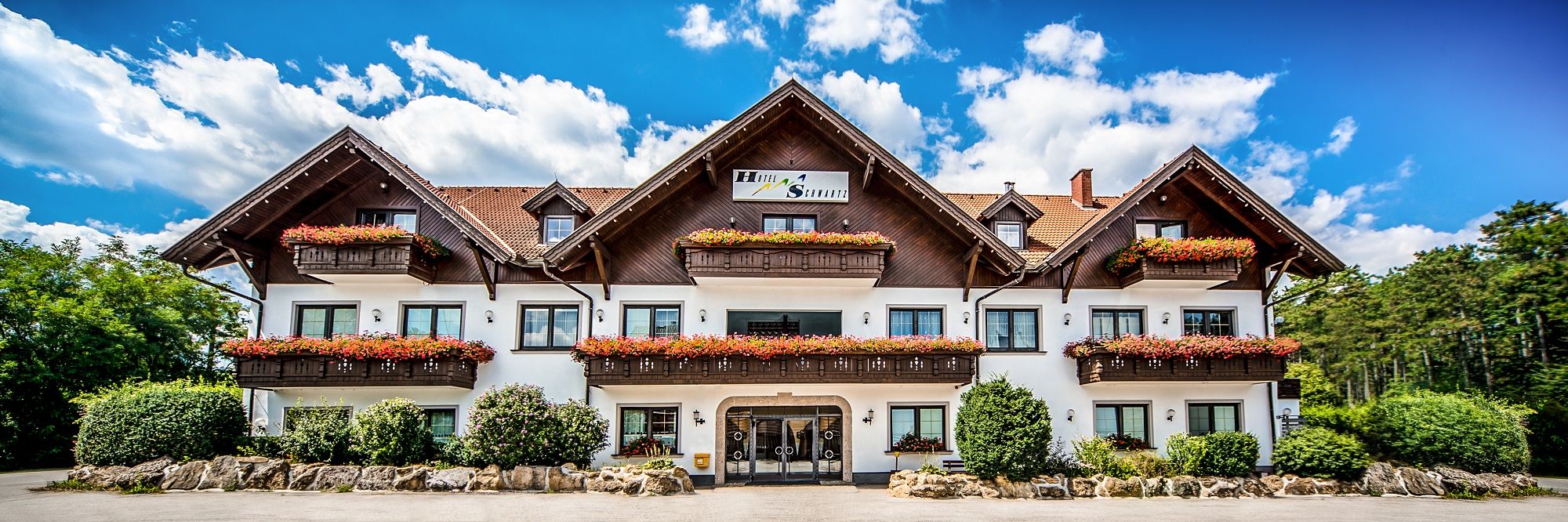 Tradiční hotel s dřevěnými balkony a květinovými truhlíky na pozadí modré oblohy.