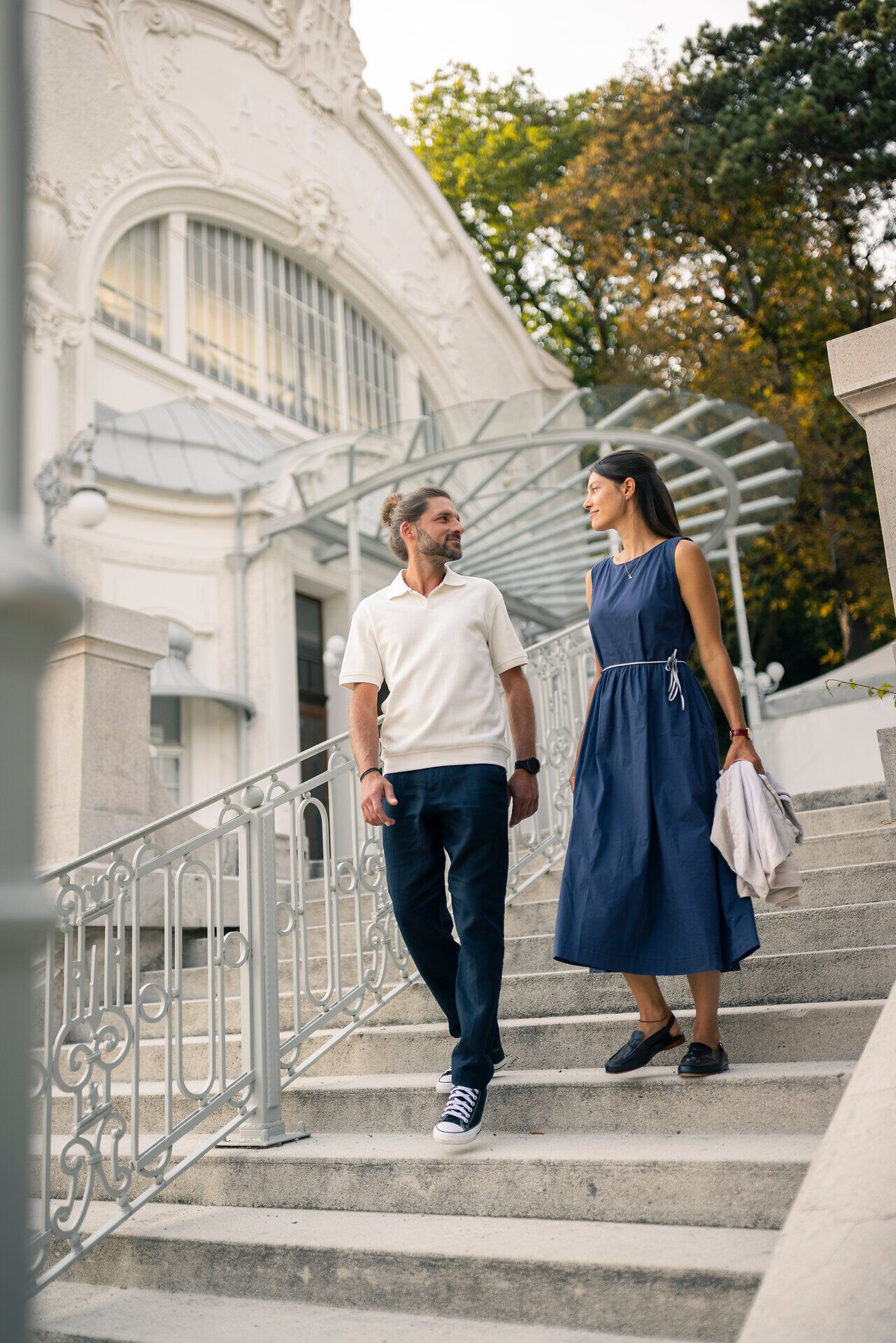 Nach einer Veranstaltung verlässt ein Paar die historische Sommerarena Baden. Sie schlendern fröhlich die imposanten Stufen des beeindruckenden Bauwerks hinab.