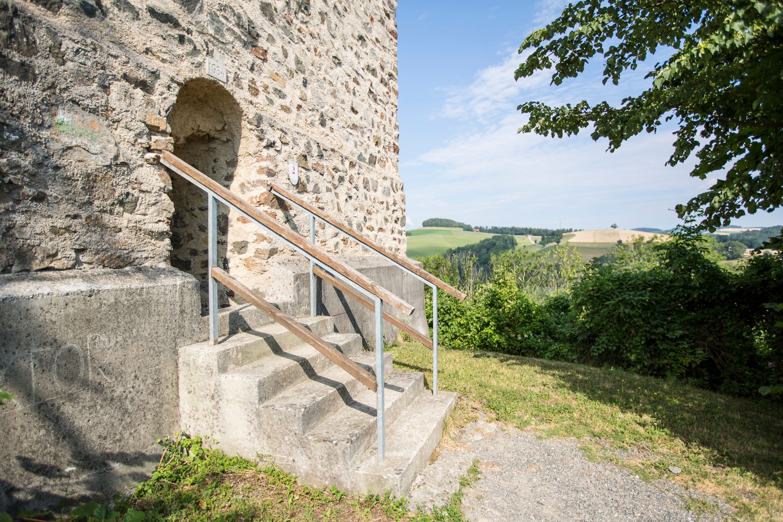 Vstup do požární věže zříceniny hradu Kirchschlag se schody a krajinou v pozadí.