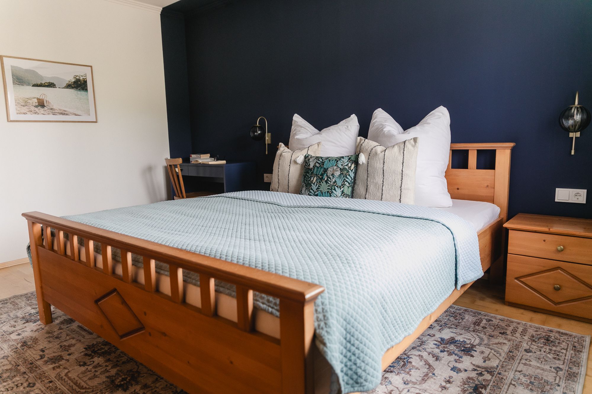 Útulná ložnice s dřevěnou postelí, modrou stěnou a dekorativními polštáři.
