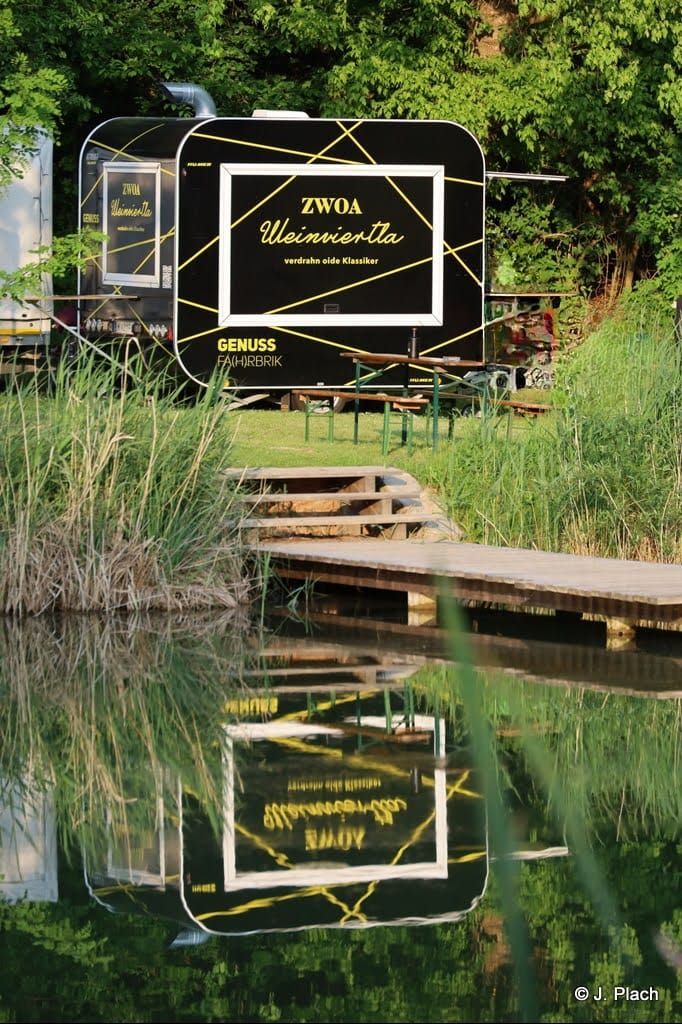 Černý kamion s nápisem "ZWOA Weinviertla" stojí v zeleném prostředí a odráží se ve vodě.