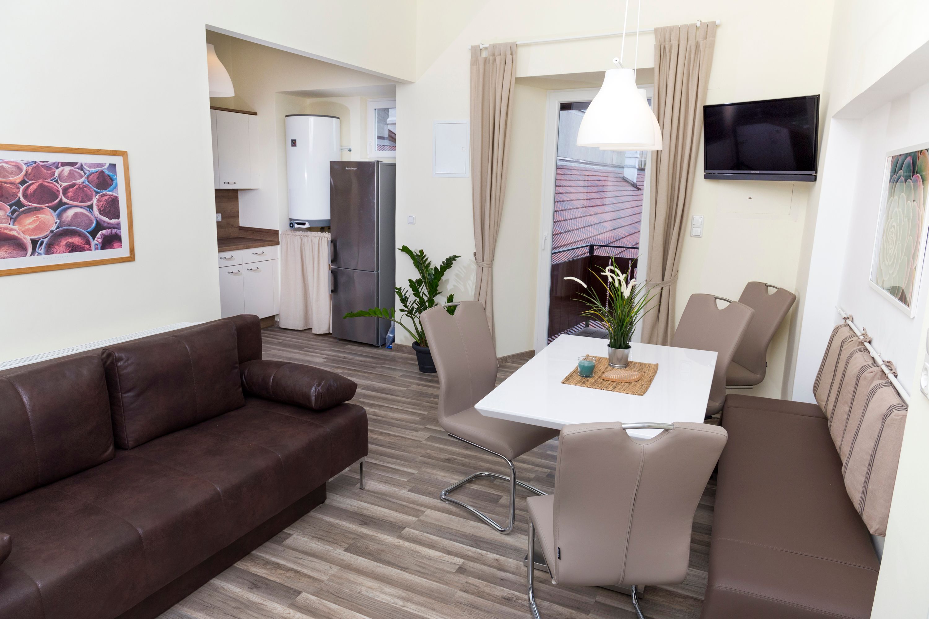 Moderní kuchyně s hnědou pohovkou, jídelním stolem a židlemi, lednicí a rostlinami.