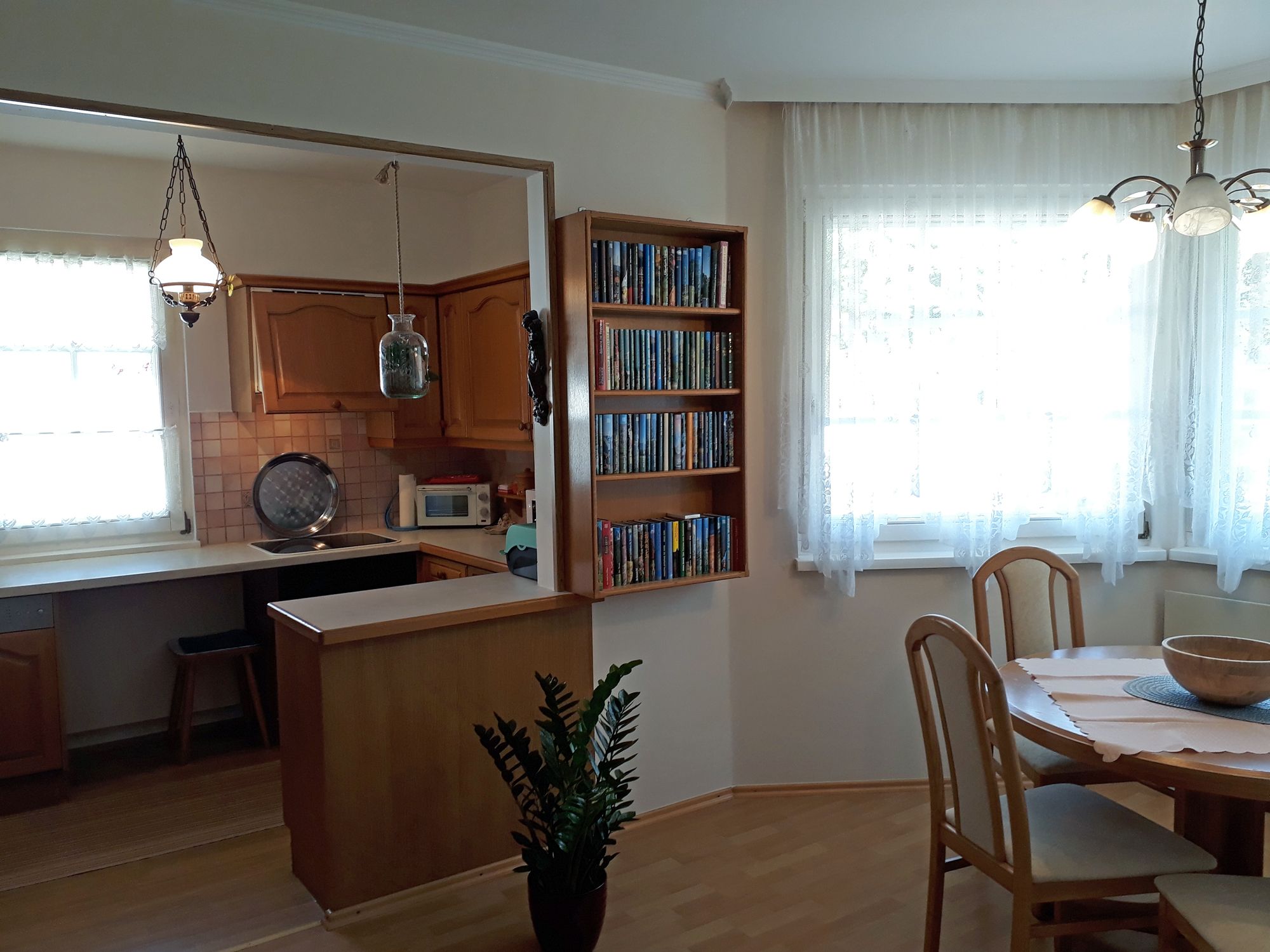 Útulná kuchyně s dřevěným nábytkem, jídelním stolem a knihovnou.