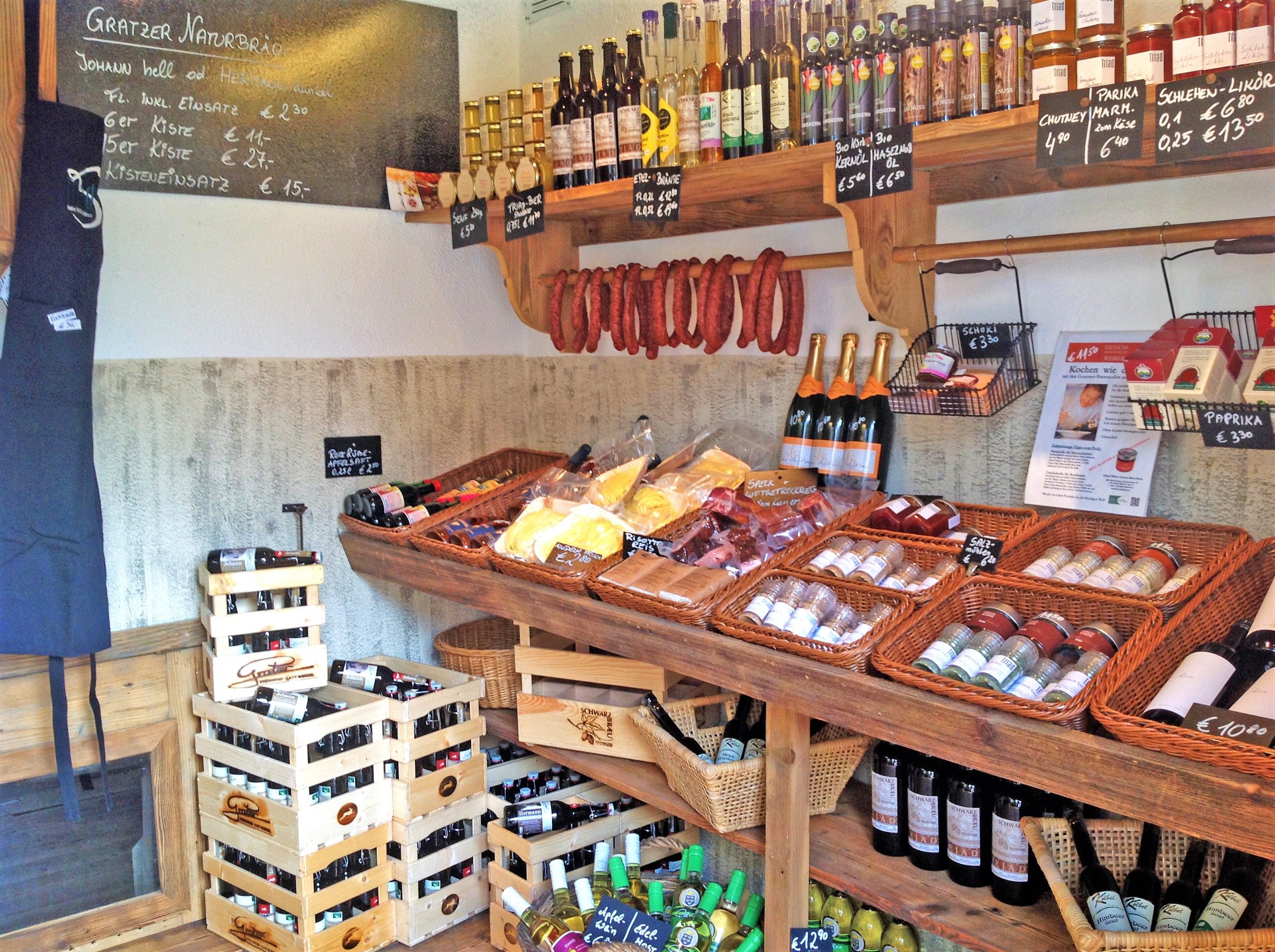 Pohled do interiéru farmářského obchodu s regály plnými regionálních produktů, jako je víno, klobásy, koření a olej.