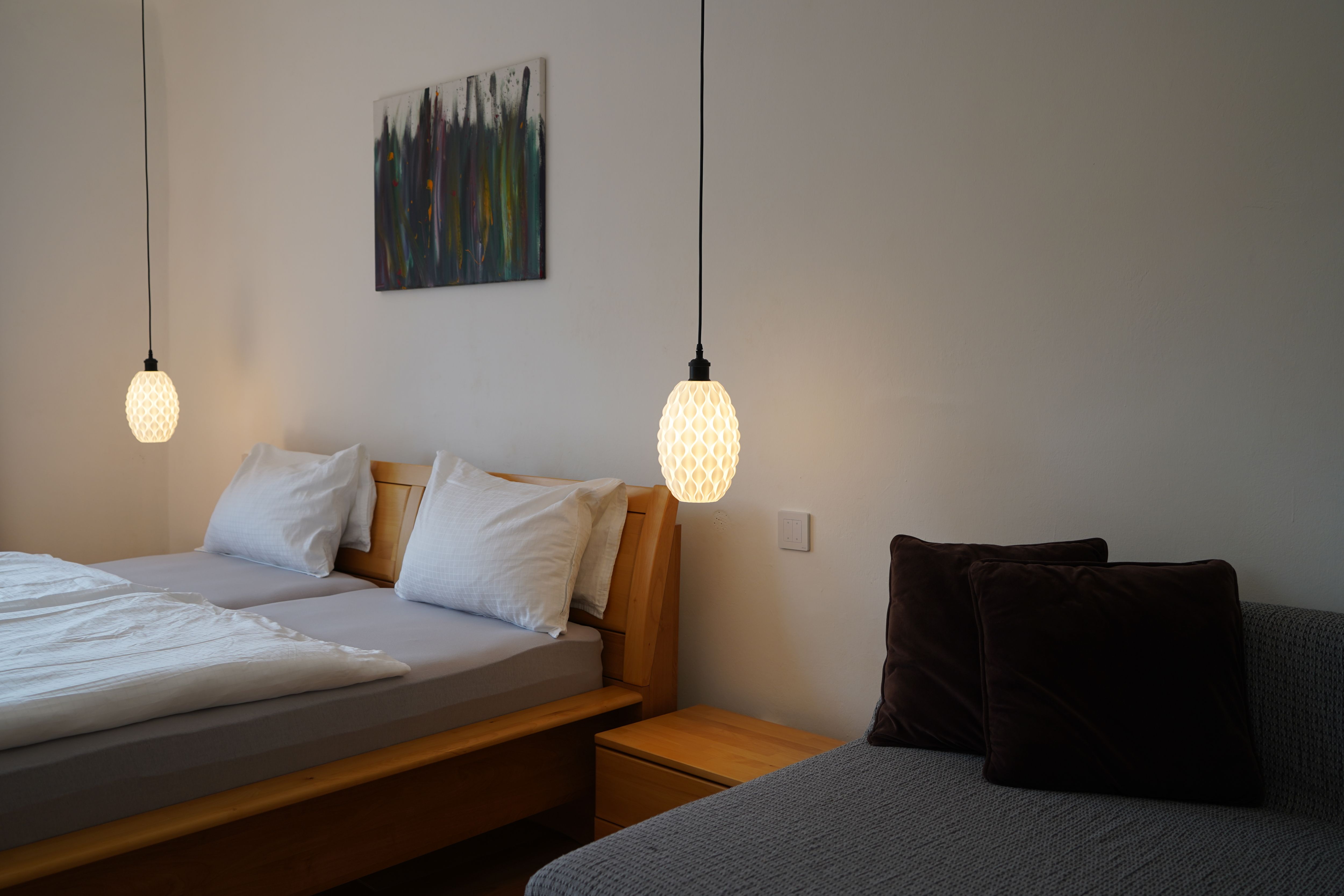 Ložnice s manželskou postelí, dvěma závěsnými lampami a pohovkou s polštáři.