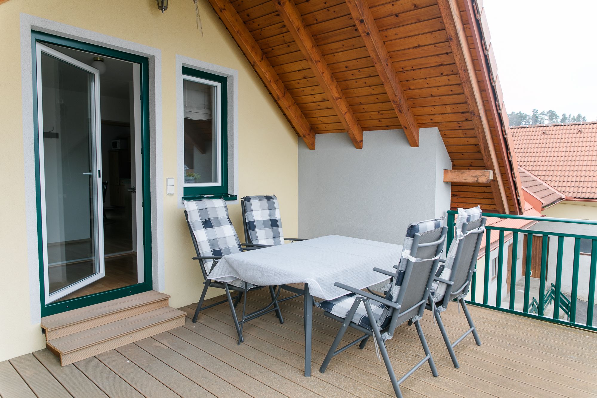 Střešní terasa se stolem a židlemi pod dřevěnou střechou.